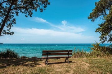 Obraz premium Wooden seat near ocean water with sky and greenery in summer
