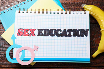 Notebooks with phrase Sex Education, paper female and male gender symbols, banana with condom on...