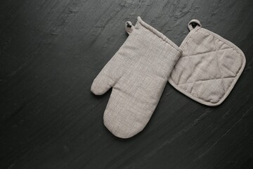 Grey oven glove and potholder on dark textured table, flat lay. Space for text