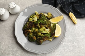 Tasty fried broccoli, shakers and lemon on light grey table, flat lay