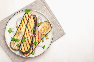 Slices of grilled eggplant, parsley, pumpkin seeds and onion on white table, top view. Space for text