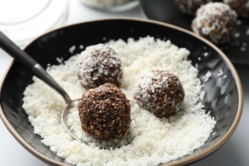 Making tasty chocolate candies with nuts and coconut flakes at white table, closeup