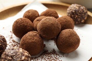 Tasty chocolate candies with cocoa powder on light table, closeup