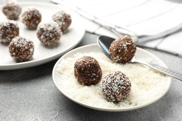 Making tasty chocolate candies with coconut flakes at grey table, closeup