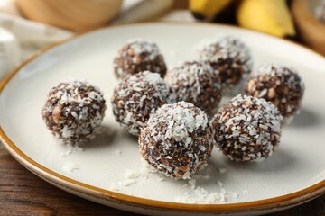 Tasty chocolate candies with nuts and coconut flakes on wooden table, closeup