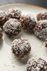 Tasty chocolate candies with nuts and coconut flakes on plate, closeup