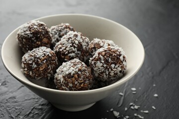 Tasty chocolate candies with nuts and coconut flakes in bowl on black table, closeup