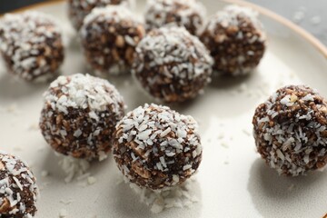 Tasty chocolate candies with nuts and coconut flakes on plate, closeup