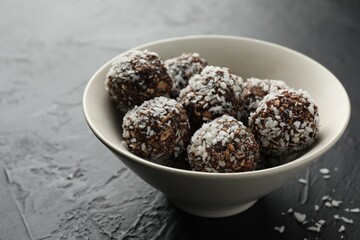 Tasty chocolate candies with nuts and coconut flakes in bowl on black table, closeup