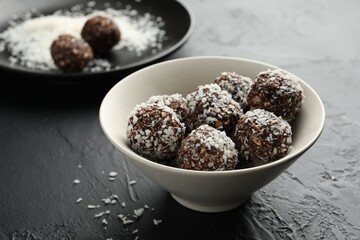 Tasty chocolate candies with nuts and coconut flakes in bowl on black table, closeup