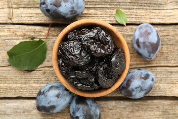 Dried prunes and fresh plums on wooden table, flat lay