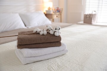 Stack of clean towels and cotton flowers on bed linens at home, closeup. Space for text