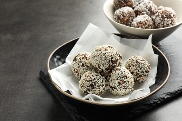 Tasty chocolate candies with nuts, sesame seeds and coconut flakes on grey table, closeup