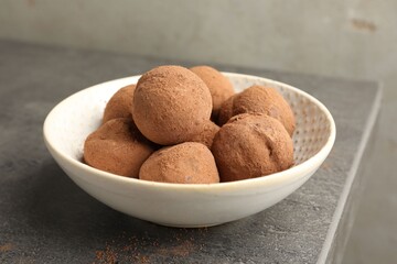 Tasty chocolate candies with cocoa powder in bowl on grey table, closeup