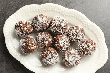 Tasty chocolate candies with nuts and coconut flakes on grey table, top view