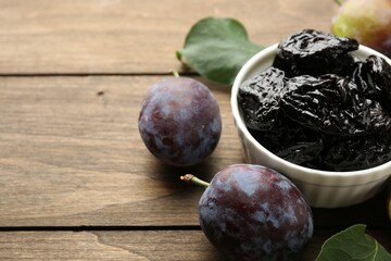 Dried prunes, fresh plums and green leaves on wooden table, closeup. Space for text