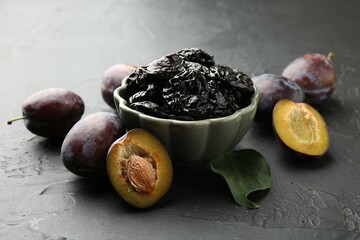 Dried prunes, fresh plums and green leaf on black table, closeup