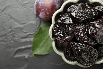 Dried prunes, fresh plum and green leaf on black table, flat lay. Space for text