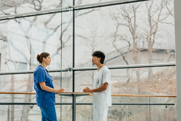 Male and female nurse discussing during break time while standing at table in corridor at hospital
