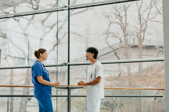 Male and female nurse discussing during break time while standing at table in corridor at hospital