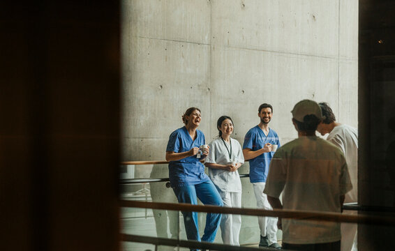 Happy male and female medical professionals enjoying coffee break in corridor seen through glass wall