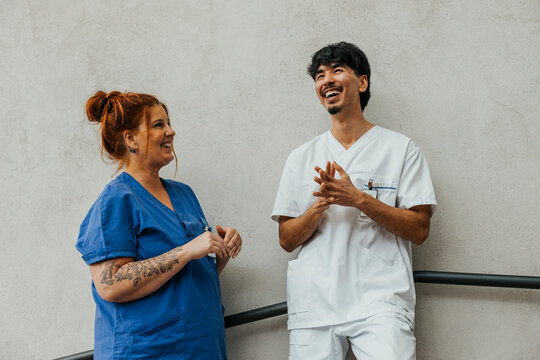 Happy male healthcare worker spending leisure time talking with female coworker while standing near wall in hospital