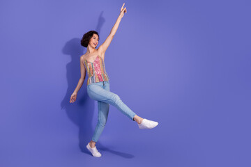 Obraz premium Crazy woman in a shiny sequin top and jeans dancing joyfully against a vibrant purple background
