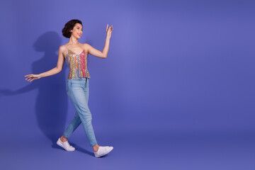 Stylish young woman in sequin top posing joyfully on purple background, showcasing modern fashion and vibrant energy