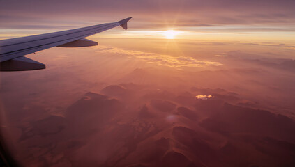 Fototapeta premium Airplane Wing with Sun Setting Behind Mountainous Terrain