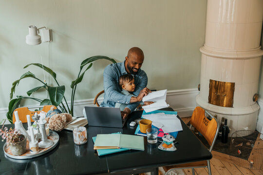 Male freelancer examining documents while sitting with son at home