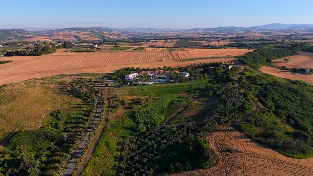 Aerial video showing approach to Mediterranean style villa surrounded by palm trees, agricultural fields and rural countryside landscape 