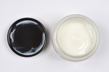 An open jar of white hair mask and its black lid are shown on a light background