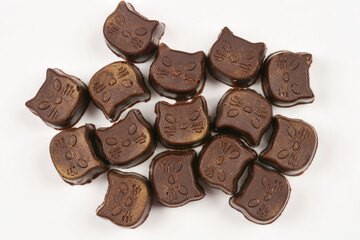 A cluster of homemade cat-shaped chocolate pralines, decorated with golden speckles, is arranged on a white surface