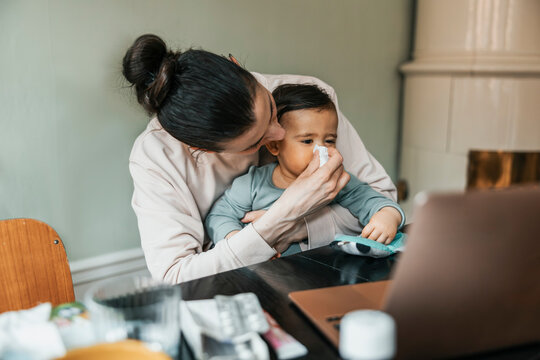 Mother blowing nose of sick baby boy at home