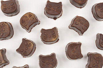 A scattered group of homemade cat-shaped chocolate pralines with golden dust lies on a white background