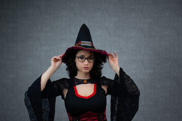 Charming witch in black and red costume, holding witch's hat with both hands over her head. Ideal for Halloween, trick or treat, fantasy october holiday. Horizontal studio portrait with copy space.