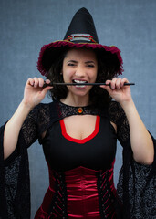 Angry witch biting her magic wand, worried about Halloween spells. Perfect for trick or treat, fantasy, witchcraft and enchantment. Studio portrait with blue background.