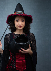 Funny witch holding magic wand and empty cauldron. Perfect for Halloween, potion brewing, trick or treat, fantasy or october holiday. Vertical studio portrait with copy space.