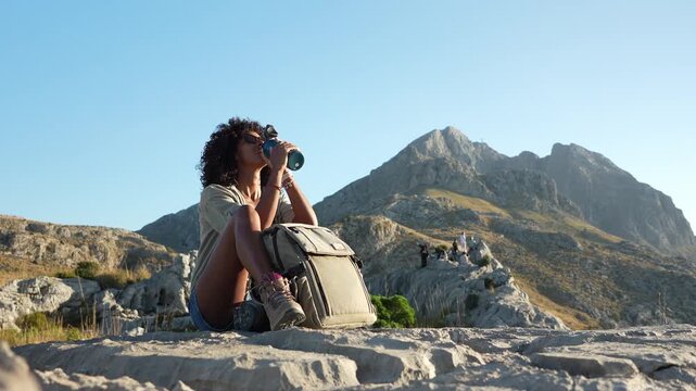 Young woman drinks water while resting during a hike in Sierra de Tramuntana, Majorca. Concept of wellness, lifestyle, exploration.