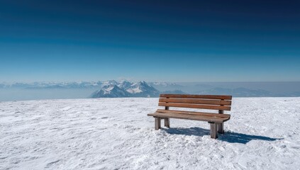 Wooden park bench atop a snow-covered mountain peak, panoramic view of distant snow-capped mountains under a vibrant blue sky