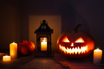 Halloween background with pumpkins, lantern, candles and fallen leaves on wooden background. Scary carved halloween pumpkin, jack o'lantern.