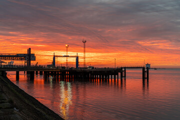 Obraz premium Fiery sunrise over the Hull passenger ferry dock with vivid orange skies reflected in calm water,