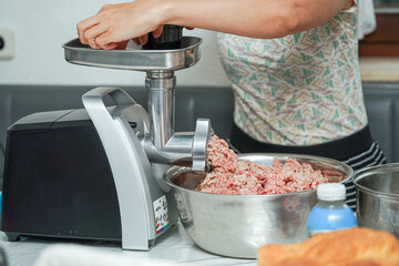 Preparing fresh ground meat in a home kitchen with an electric meat grinder during afternoon cooking session