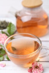 Tasty rose tea in glass cup and flowers on white wooden table, closeup
