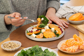 Woman eating healthy winter salad with citrus, persimmon and feta 