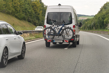 Bicycle mounted on rear of van traveling along highway with cars in motion on a cloudy day