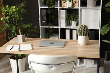 Stylish workplace with laptop, stationery and floral decor in office. Biophilic interior design