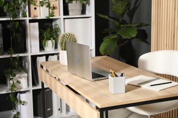 Stylish workplace with laptop, stationery and floral decor in office. Biophilic interior design