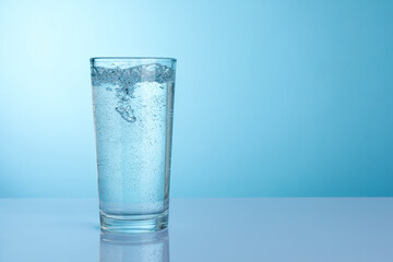 Refreshing soda water in glass on light grey mirror table against turquoise gradient background, closeup. Space for text