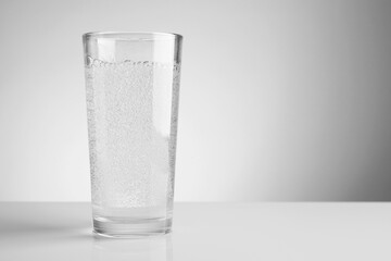 Refreshing soda water in glass on white mirror table against light grey gradient background, closeup. Space for text